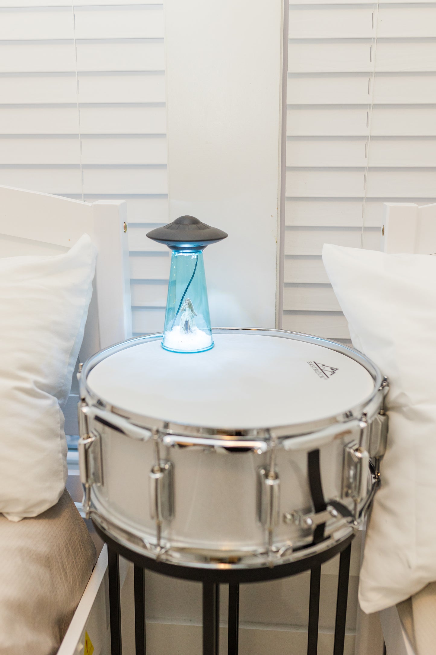 Silver snare drum with a glowing blue top on a stand against a white wall.