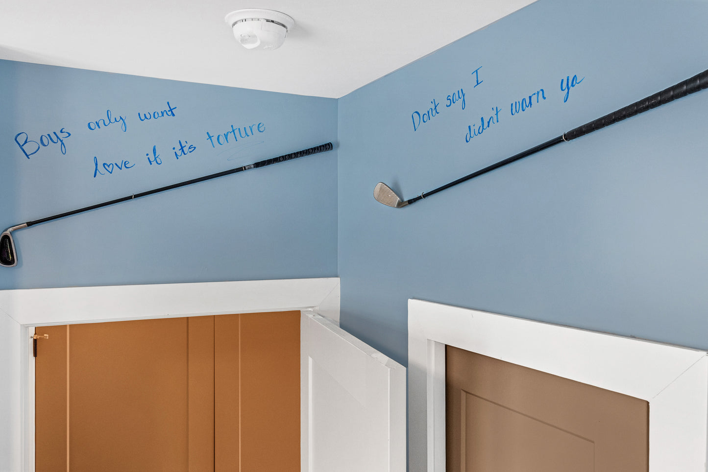 Two golf clubs mounted on a blue wall with text, in a room with wooden doors.
