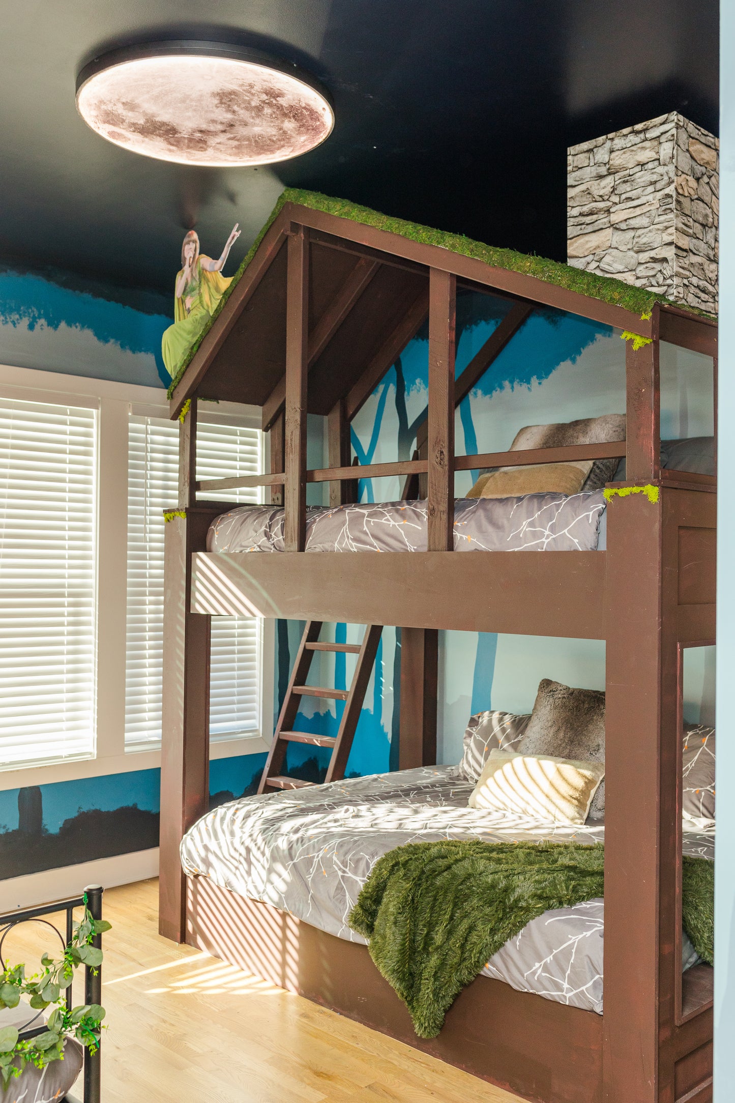Bunk bed with green grass-like roof in a room with blue walls and a stone fireplace.