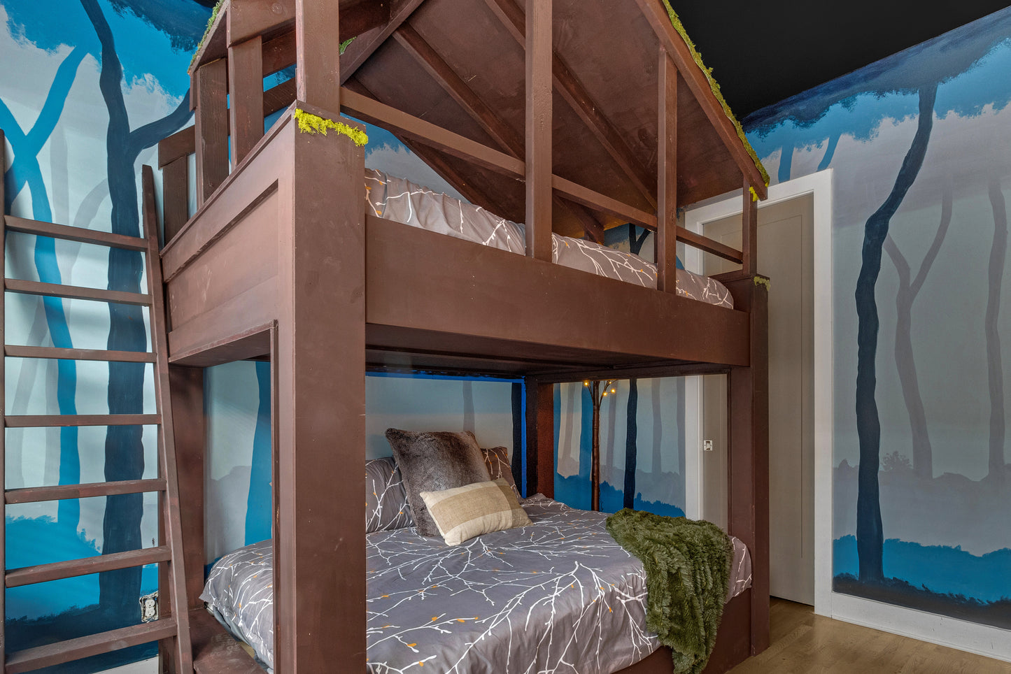 Wooden bunk bed with a mural of trees on the wall in a child's bedroom.