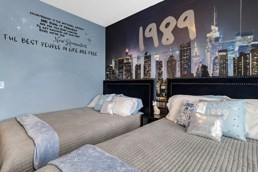 Two beds in a room with a '1989' themed wall mural of a city skyline.