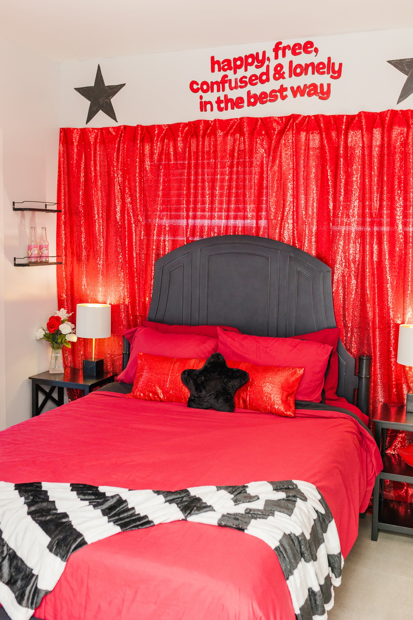 Bedroom with red bedding, black headboard, and decorative text on a red curtain.