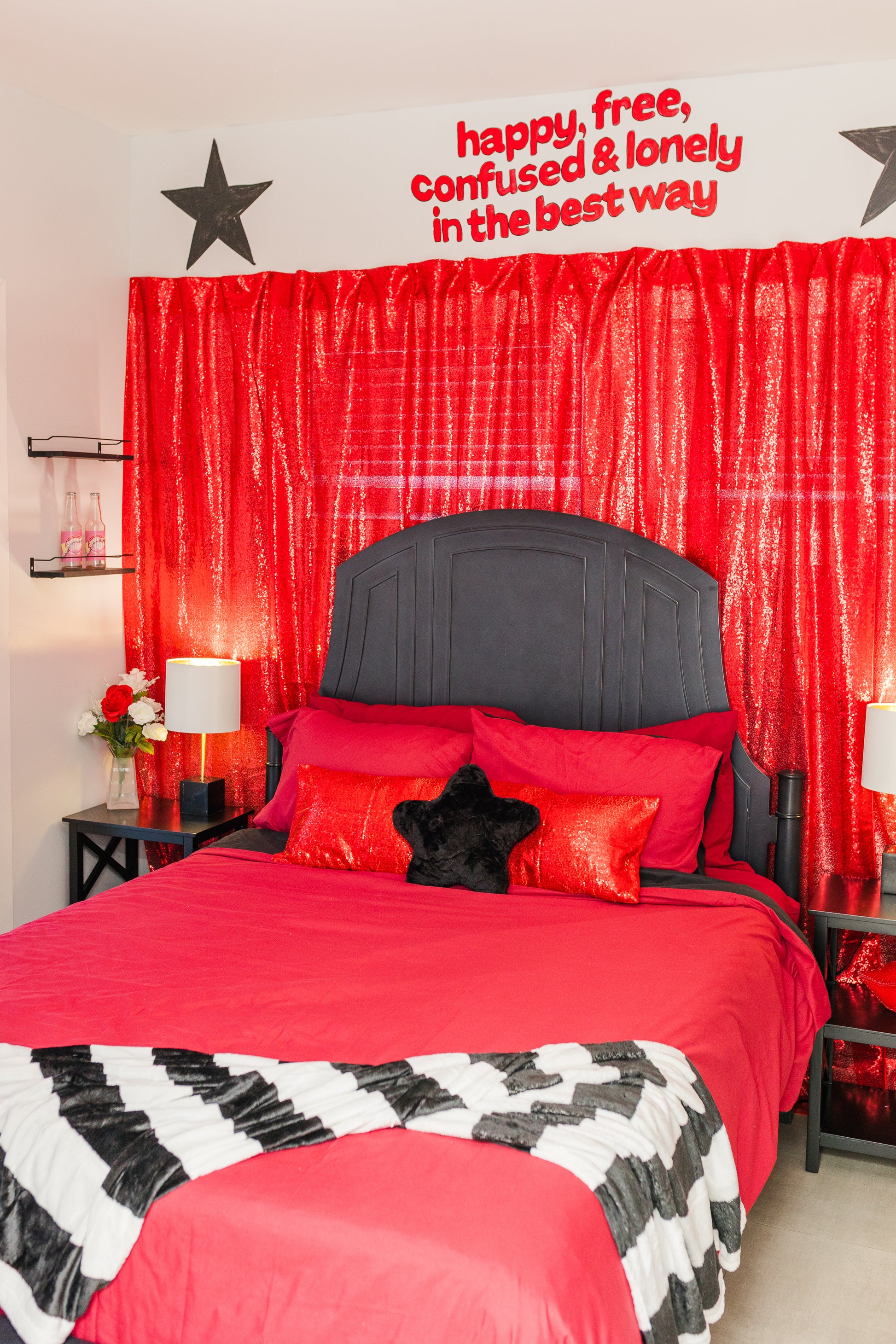 Bedroom with red bedding, black headboard, and decorative text on a red curtain.