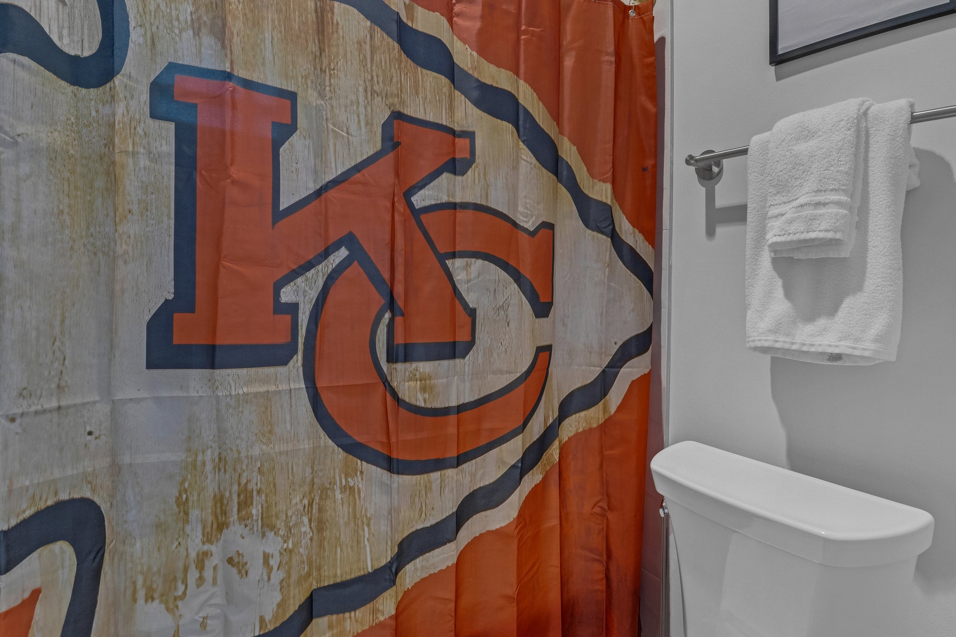 Bathroom with a shower curtain featuring a logo and a white toilet.