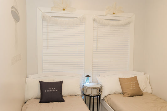 Two beige couches with pillows against a wall with window blinds